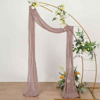 Sheer mauve fabric draped elegantly over a gold wedding arch with floral accents.