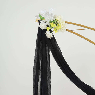 Black chiffon drape adorned with artificial flowers on a golden arch.