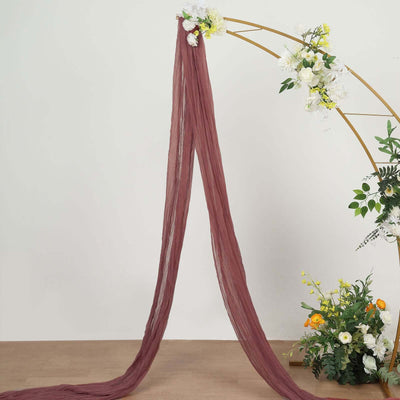 Burgundy sheer drapery fabric hanging elegantly from an arch with floral accents.