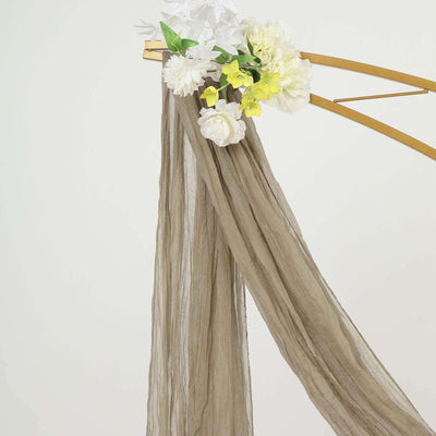 Sheer brown fabric draped with white and yellow flowers on a gold stand