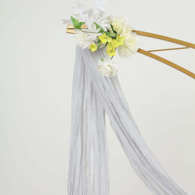 White draped fabric adorned with faux flowers on a gold arch