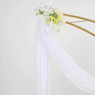 White draped fabric with floral accents on a gold arch.
