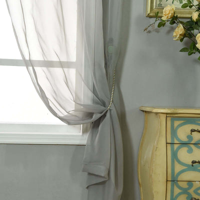 Sheer gray curtain elegantly draped by a window with floral decor.