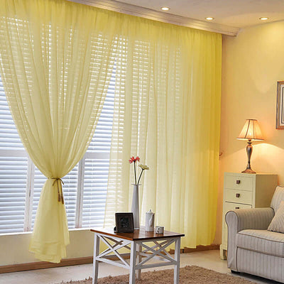 Yellow sheer curtains in a cozy living room setting with a lamp and coffee table.