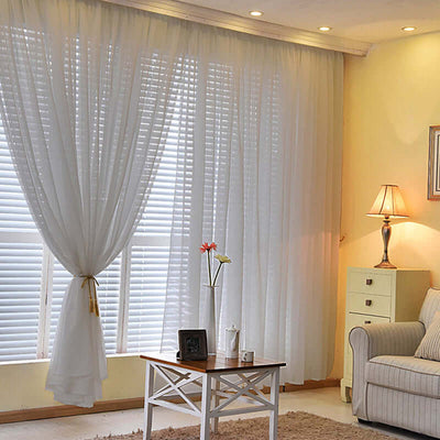 Sheer white curtains draping a window with a cozy living room setup.