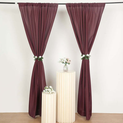 Burgundy sheer curtains draped elegantly on two white stands with flowers.