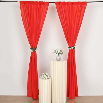 Red curtains with floral tiebacks draped on a rod over white pedestals.