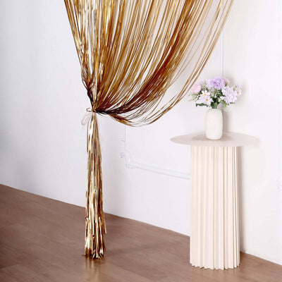 Gold metallic fringe curtain with flowers in a vase on a modern pedestal table.