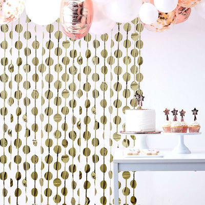 Gold circle party backdrop with balloons and a cake on a table.