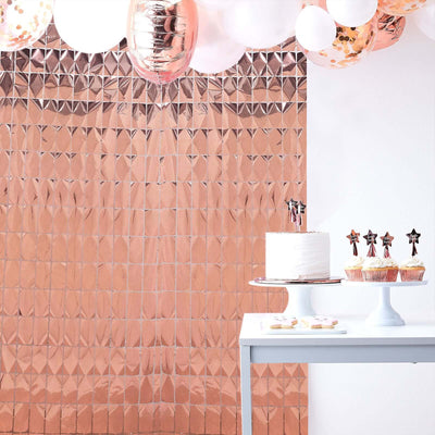 Rose gold party backdrop with cake and cupcakes on a table.