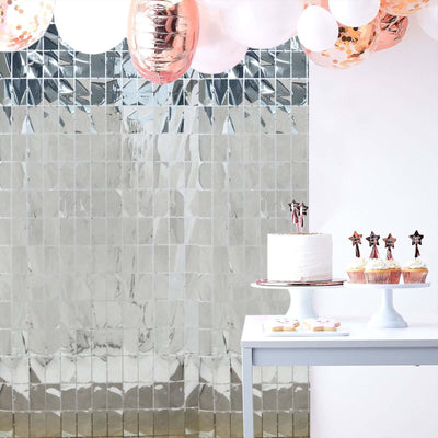 Decorative party setup with balloons, cake, and cupcakes against a shiny backdrop.