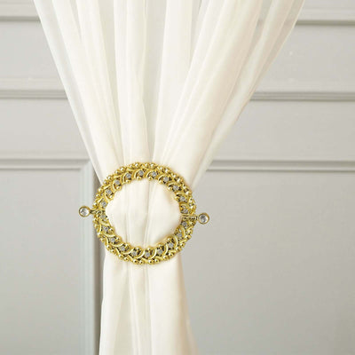 Gold curtain tieback with decorative design on white fabric.
