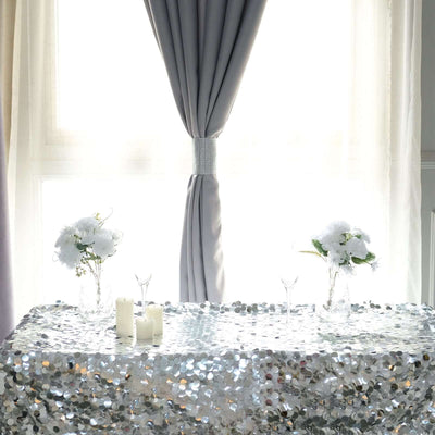 Decorative table with sequin tablecloth, flowers, and candles against a bright window.