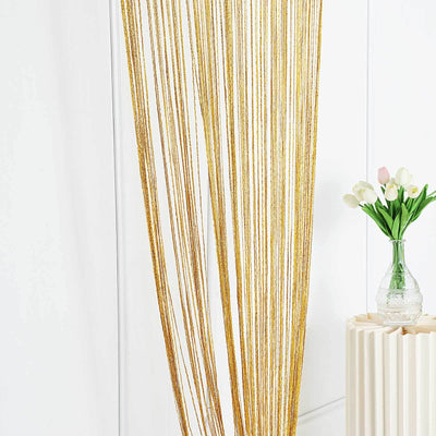 Gold beaded curtain hanging beside a vase of tulips on a table.