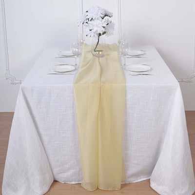 Yellow table runner on a white table setting with flowers and glassware.