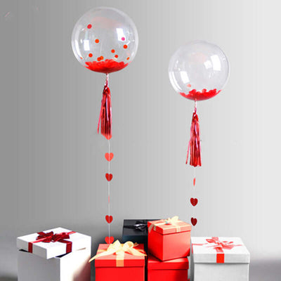 Clear balloons with red confetti, tied with tassels, above gift boxes.