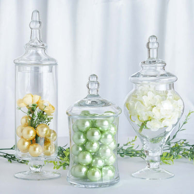 Glass apothecary jars with decorative fillers in gold, green, and white.