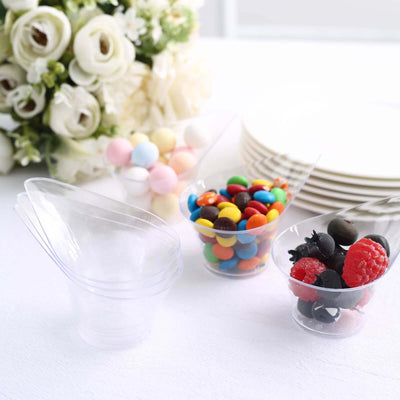 Clear plastic dessert cups with colorful candies and berries on a table.