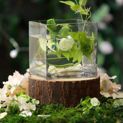 Clear glass vase with greenery and flowers on a wooden stump.