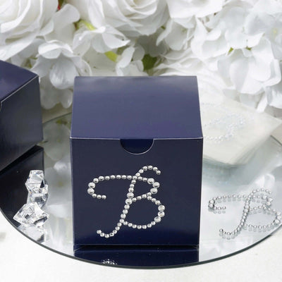 Navy blue gift box with rhinestone letter "B" design on mirrored surface.