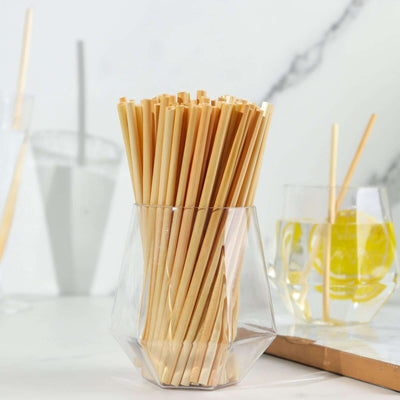 Bamboo straws in a clear glass holder on a marble countertop.