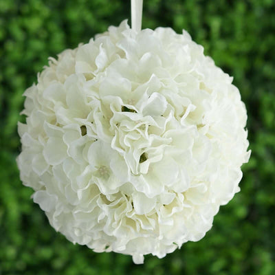 White floral ball decoration hanging against greenery backdrop.