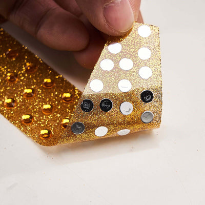 Gold glitter adhesive ribbon with silver and black dots, held by hand.