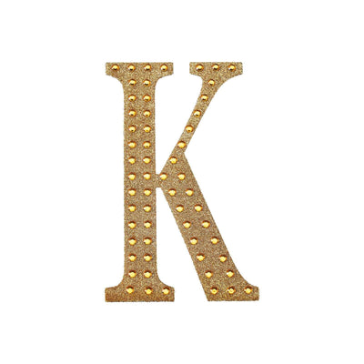 Gold letter "K" with studded embellishments on a white background.