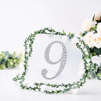 Decorative table number 9 surrounded by greenery and flowers on a white background