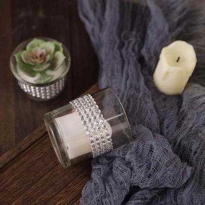 Decorative candle in a glass holder with rhinestone accents on a textured fabric backdrop.