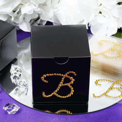 Black gift box with rhinestone "B" design on a mirrored surface.