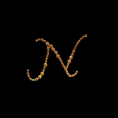 Gold decorative letter N made of beads on a black background.