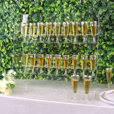 Acrylic drink display with champagne glasses on a table against green foliage backdrop.