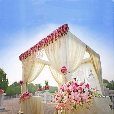 Elegant wedding canopy adorned with pink flowers and drapes against a clear blue sky.