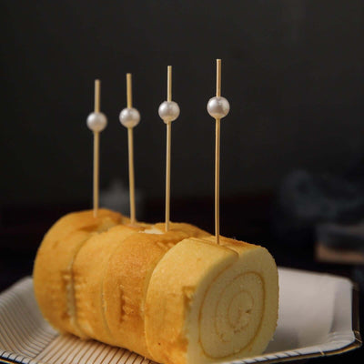 Rolled cake with decorative skewers on a plate.