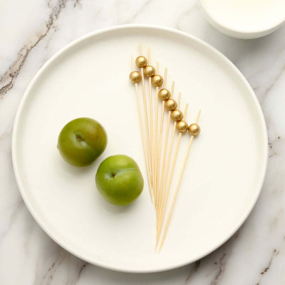 Golden cocktail picks with green apples on a white plate.