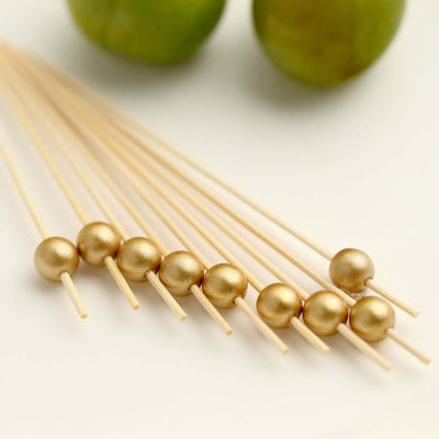 Gold cocktail picks arranged with limes in the background.