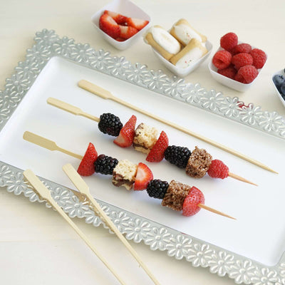 Colorful fruit and dessert skewers on a decorative platter with fresh berries.