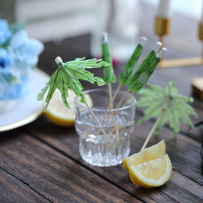Tropical drink stirrers with green palm leaves in a glass with lemon wedges.