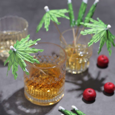 Cocktails with decorative green umbrellas and red berries on a table.