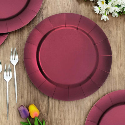 Burgundy paper plate on a wooden table with forks and flowers.