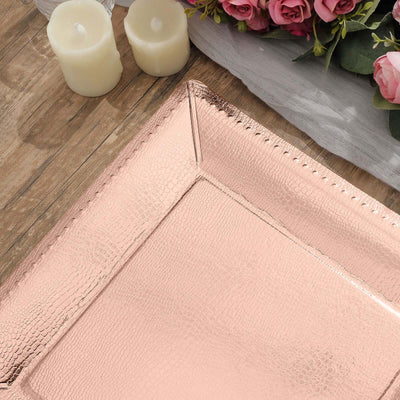 Rose gold textured serving tray on a wooden table with candles and flowers.
