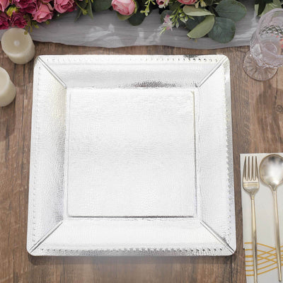 Silver square charger plate on a wooden table with floral decor.