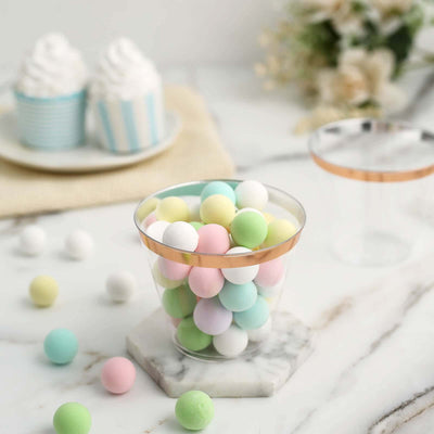 Colorful candy balls in a clear cup with a gold rim on a marble surface.