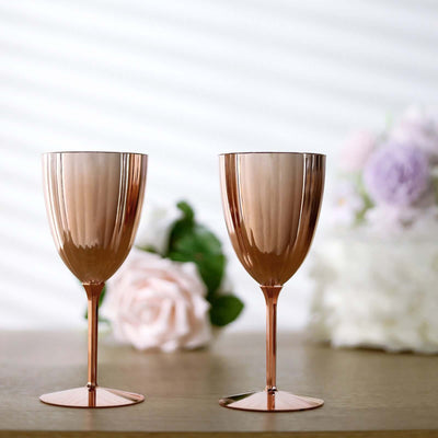 Rose gold stemmed glasses on a wooden table with floral backdrop.