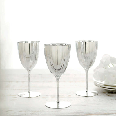 Three elegant silver wine glasses on a light wooden surface.