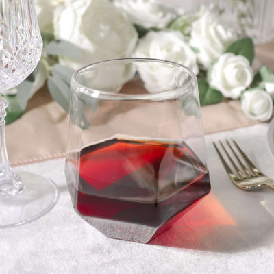 Faceted glass tumbler with dark liquid on elegant table setting.