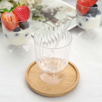 Clear glass dessert cup with spoon on a wooden plate, surrounded by fruit parfaits.