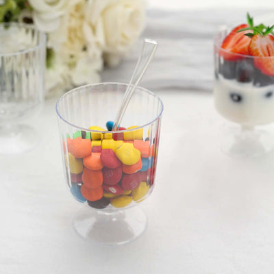 Colorful candy in a clear cup with a spoon, set against a soft background.