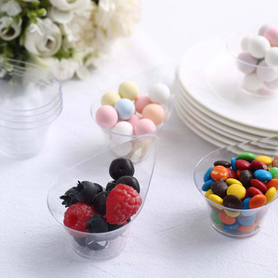 Clear plastic dessert cups with colorful candies and berries on a table.